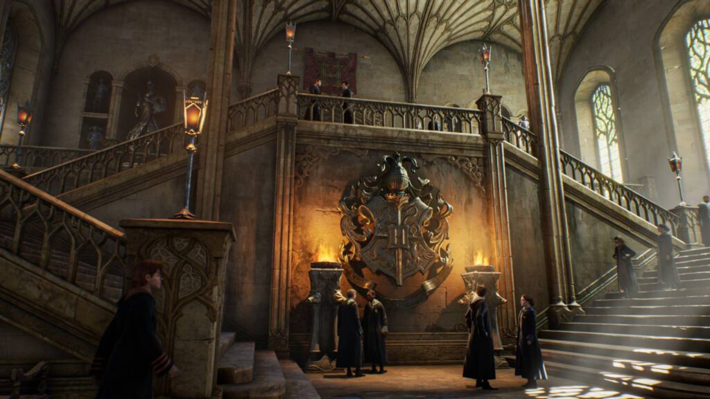 Die große Treppenhalle in Hogwarts Legacy mit dem leuchtenden Schulwappen, Schülern in Roben und den charakteristischen verzweigten Treppen.