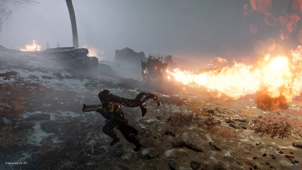Helldivers 2 zeigt Soldat im Feuergefecht gegen riesige Maschine mit Flammenwerfer in zerstörter Landschaft