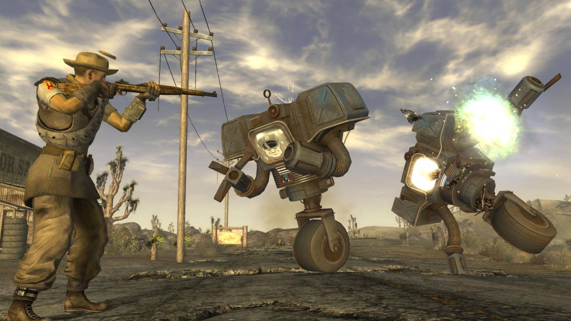 Screenshot aus Fallout: New Vegas, in dem ein bewaffneter Ranger in der Mojave-Wüste zwei Roboter auf einer Straße beschießt.