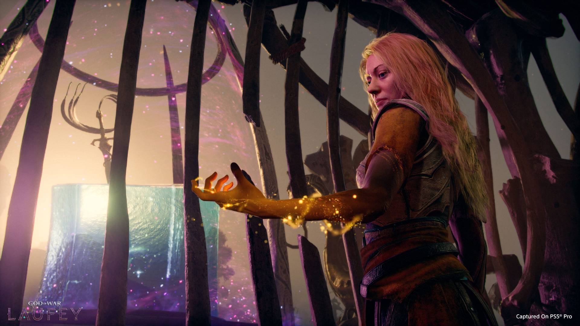 Faye aus God of War Laufey streckt in einem Knochengerüst ihre leuchtende Hand aus, während im Hintergrund ein riesiger Würfel von magischen Partikeln umgeben ist.