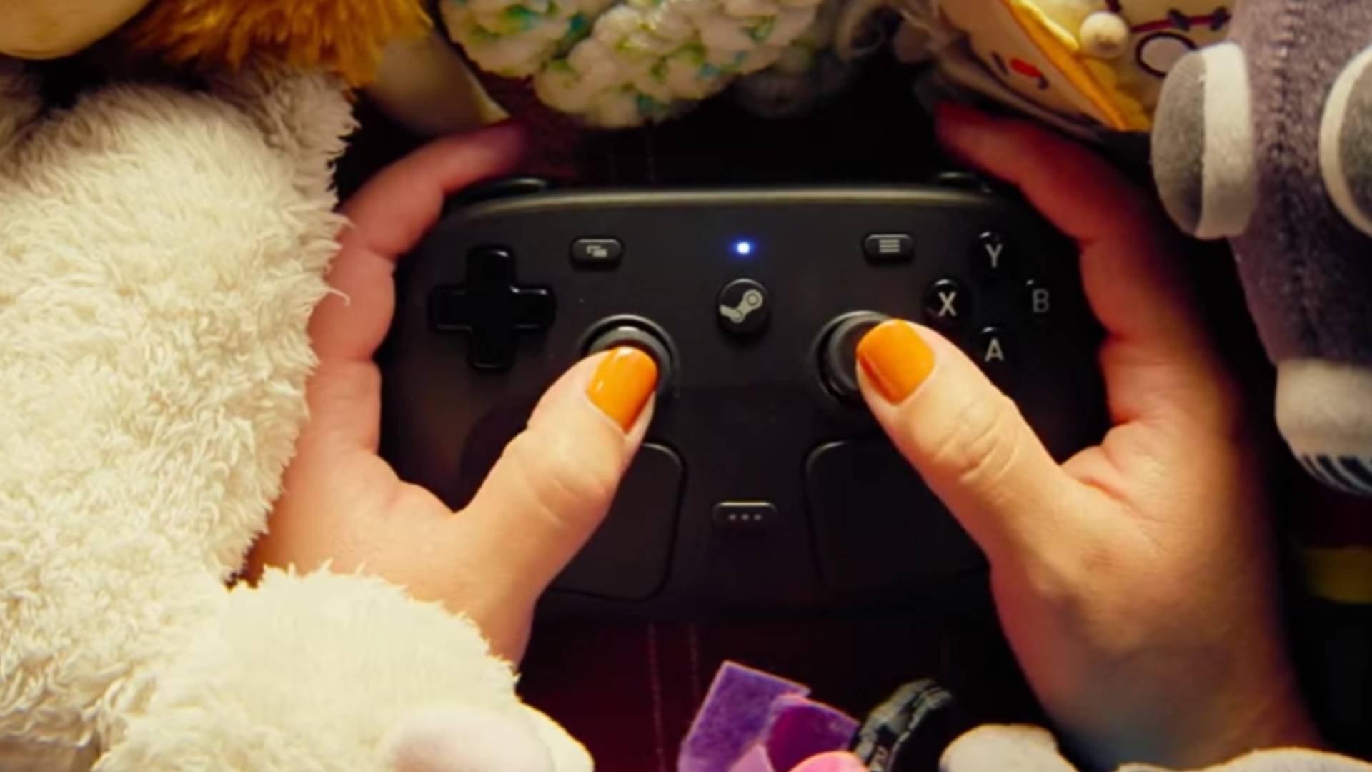 Hände halten einen schwarzen Steam Controller zwischen mehreren Plüschtieren, während die Daumen auf den Analogsticks liegen.