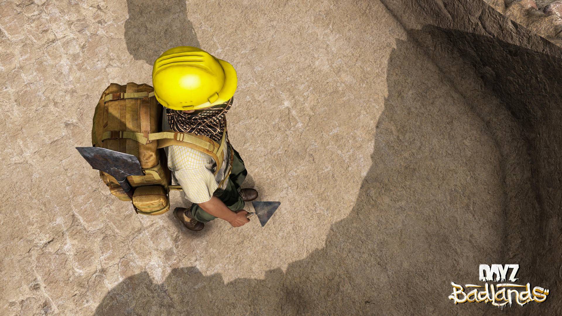 Ein Überlebender mit gelbem Bauhelm, Rucksack und Werkzeug steht in DayZ Badlands auf felsigem Untergrund.